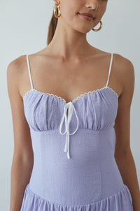 Woman wearing a light purple dress with thin straps against a plain background