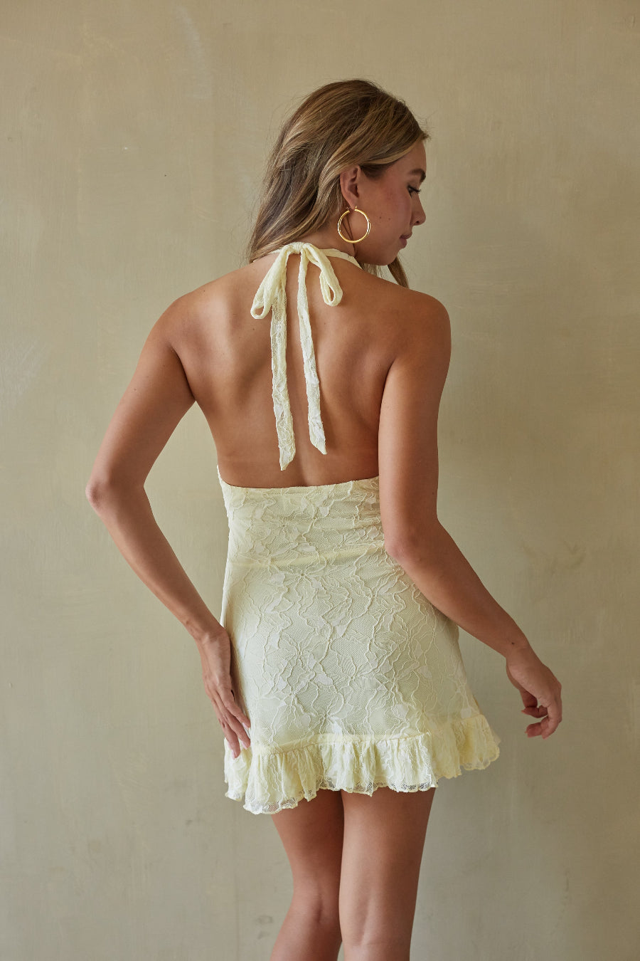 Woman wearing a light yellow halter neck dress with ruffled details against a beige background