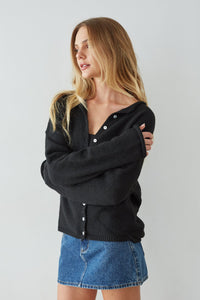 Woman wearing a black cardigan and blue denim skirt against a plain background