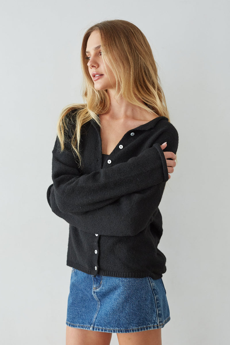 Woman wearing a black cardigan and blue denim skirt against a plain background