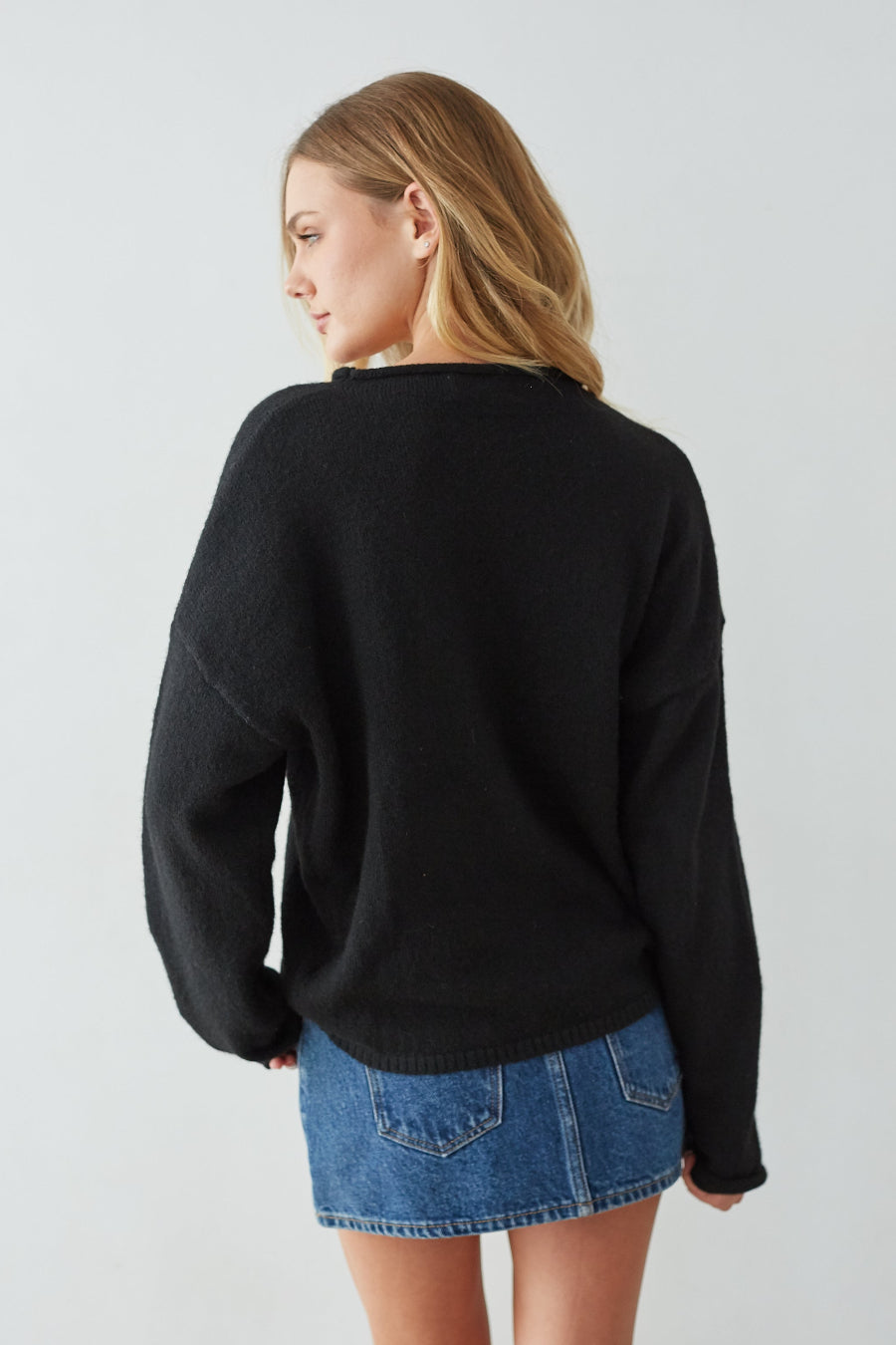 Person wearing a black sweater and denim skirt on a light gray background