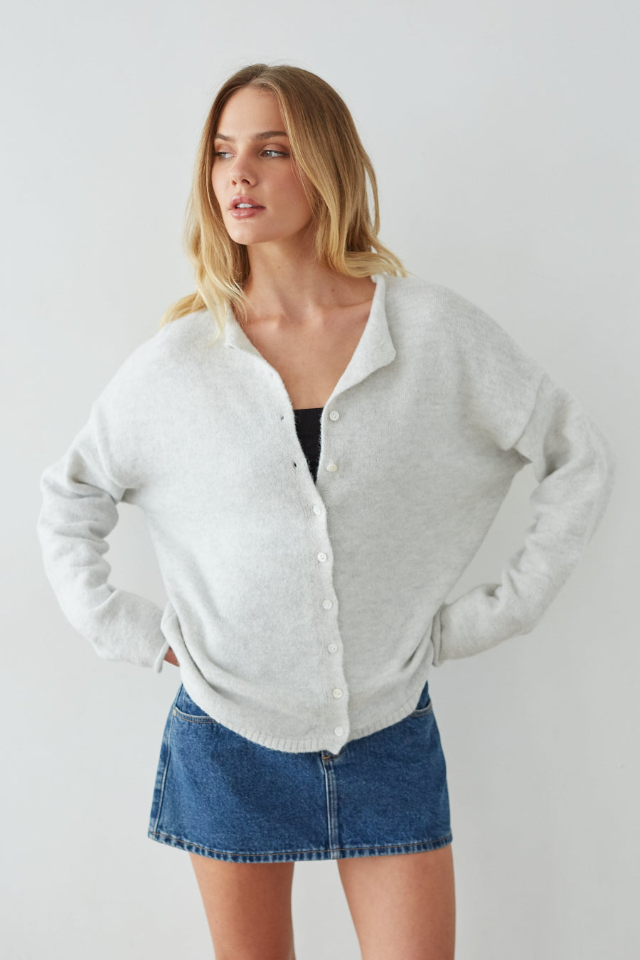 Woman wearing a light gray cardigan over a black top and blue denim skirt on a white background