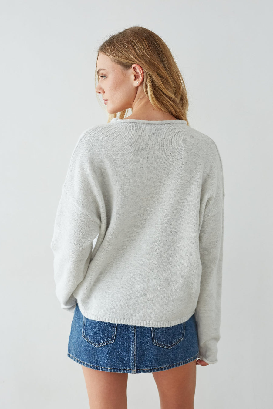 Woman wearing a gray sweater and denim skirt on a plain background