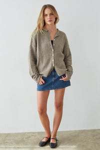 Woman wearing a green cardigan and blue denim skirt against a white background