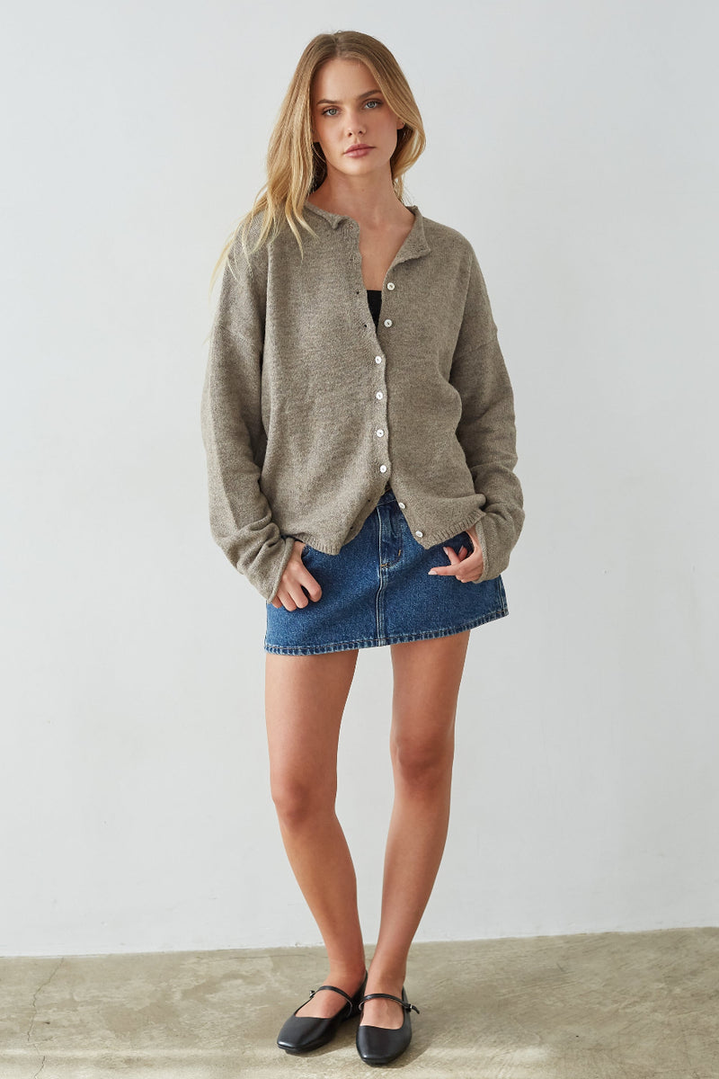 Woman wearing a green cardigan and blue denim skirt against a white background