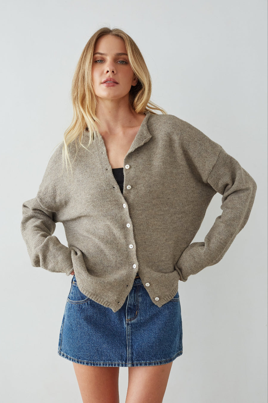 Woman wearing a beige cardigan and denim skirt on a plain background
