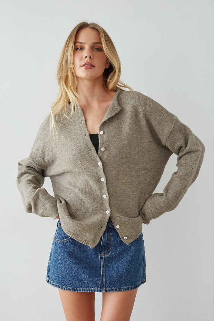 Woman wearing a beige cardigan and denim skirt on a plain background