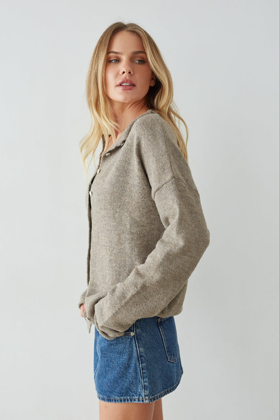 Woman wearing a brown sweater and denim skirt against a plain background