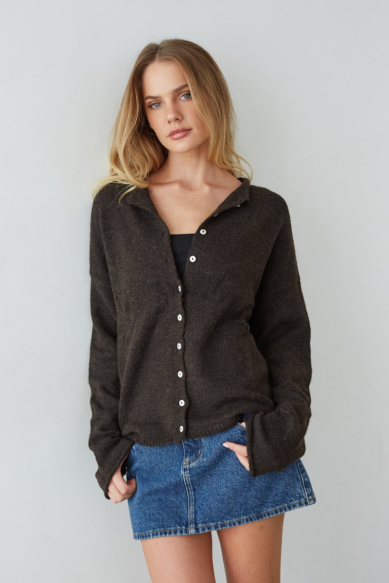 brown-image | Woman wearing a dark brown cardigan over a black top and blue denim skirt on a plain background