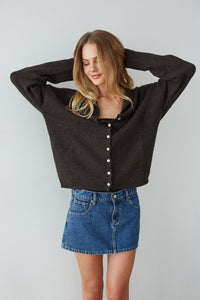 Woman wearing a dark brown cropped sweater and blue denim skirt against a plain background