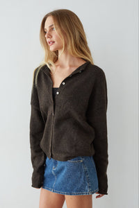 Woman wearing a dark brown jacket and blue denim skirt on a plain background