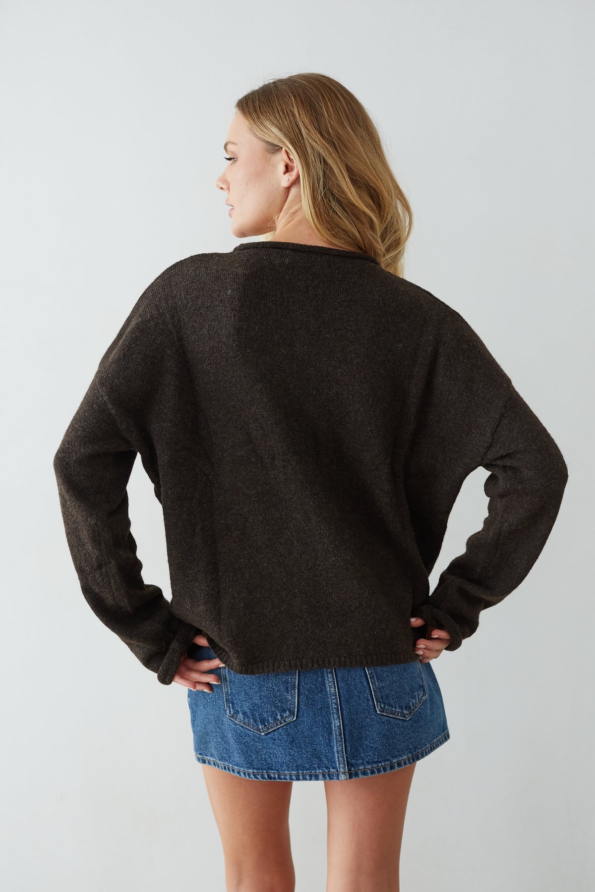 Person wearing a chocolate sweater and denim skirt on a light gray background