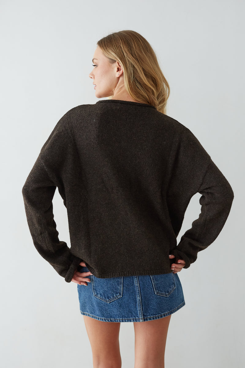 Person wearing a chocolate sweater and denim skirt on a light gray background