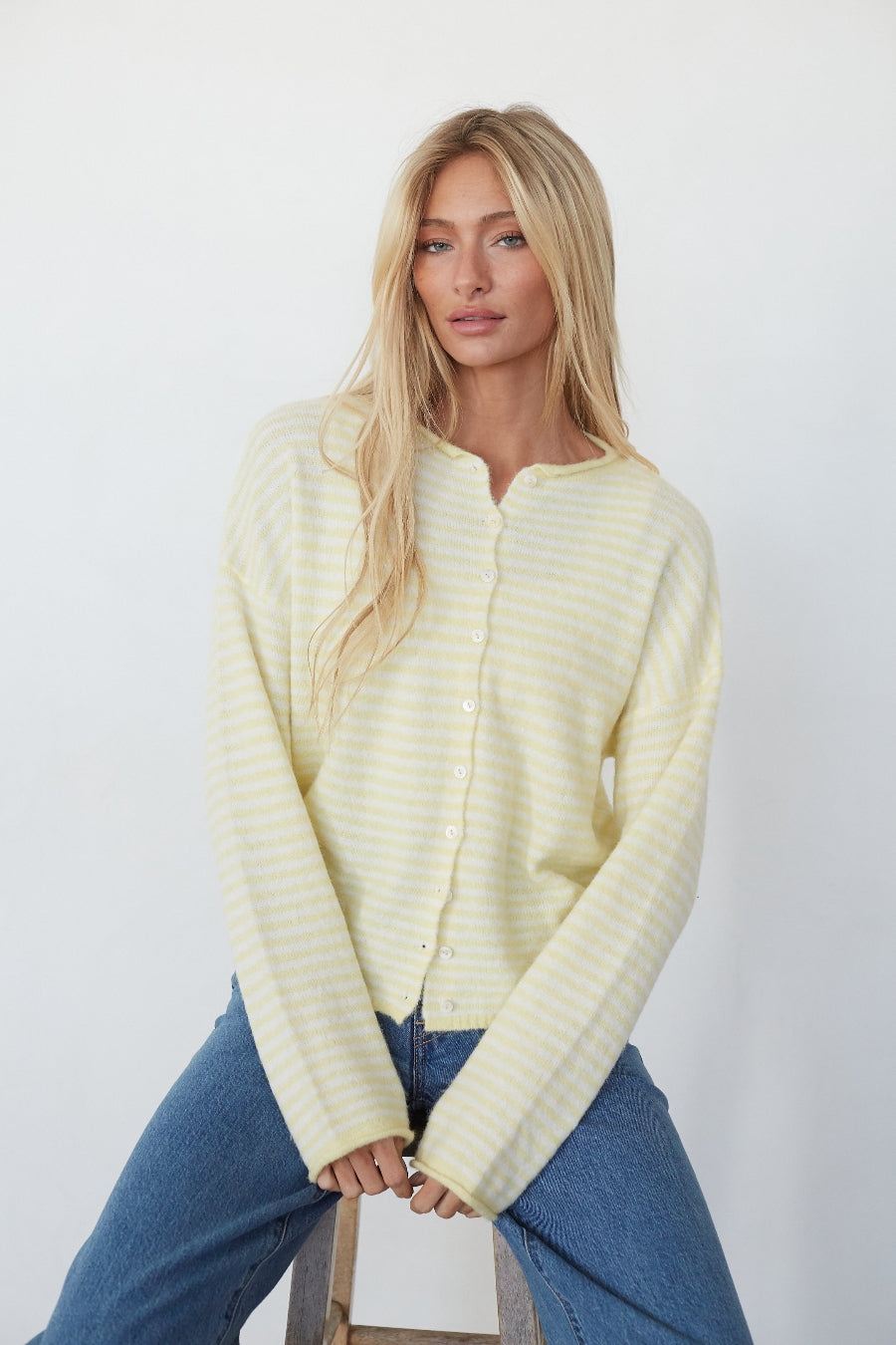 Woman wearing a light yellow ribbed sweater and blue jeans against a white background