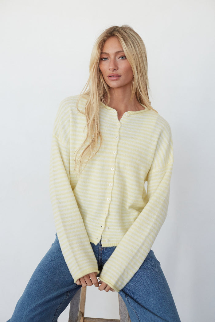 Woman wearing a light yellow ribbed sweater and blue jeans against a white background