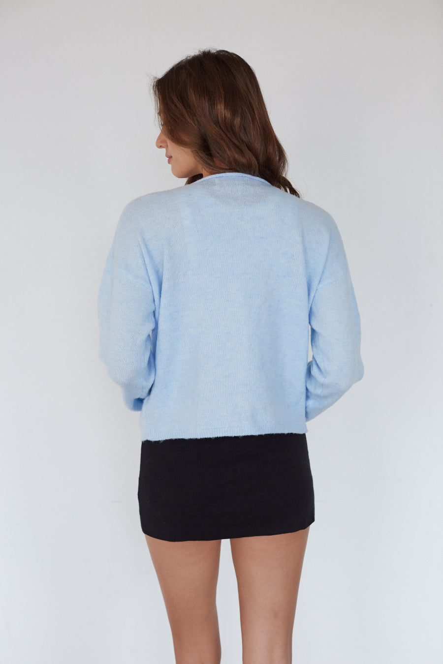 Person wearing a light blue cardigan over a black top on a white background