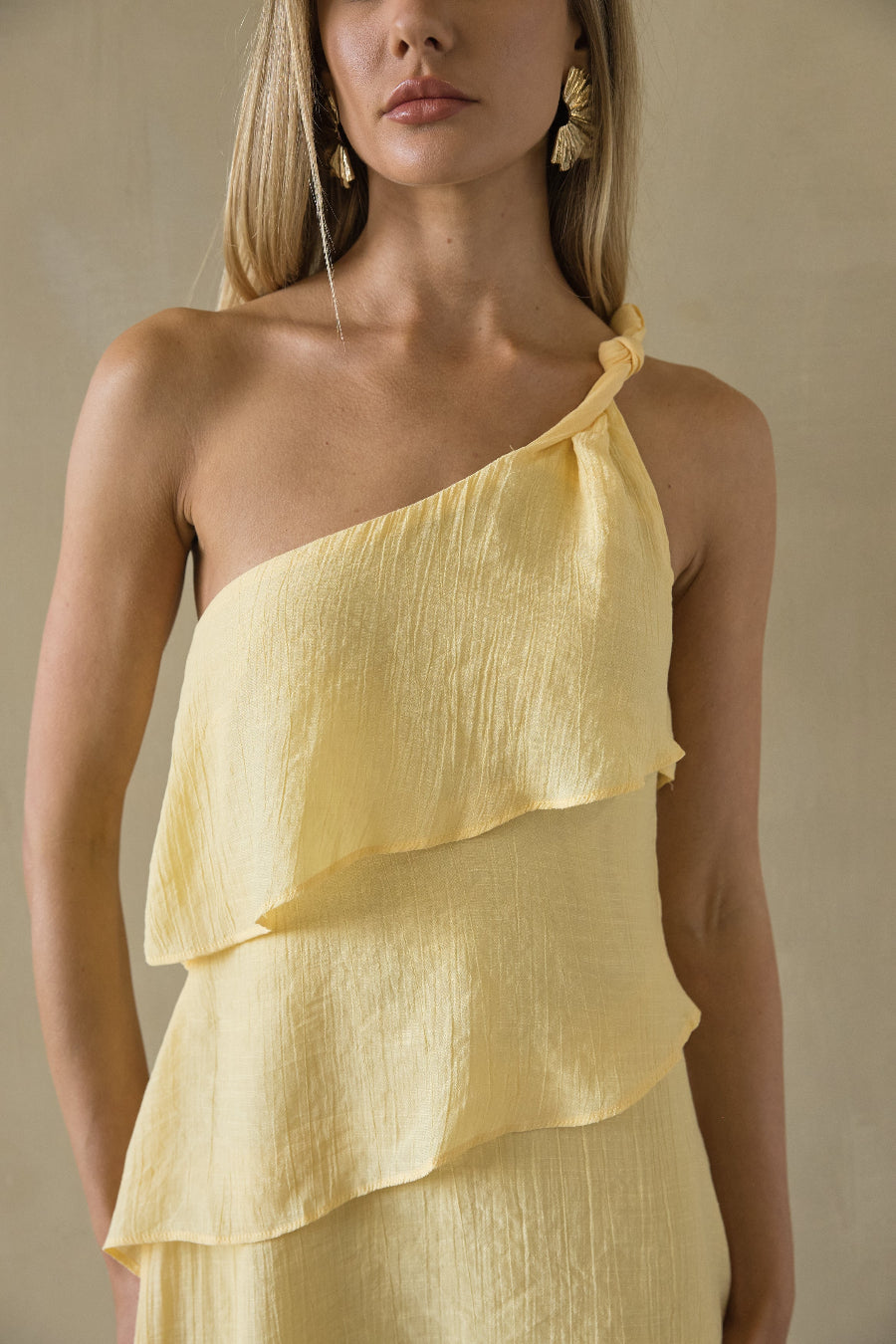Woman wearing a yellow one-shoulder dress against a neutral background