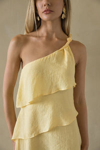Woman wearing a yellow one-shoulder dress against a neutral background