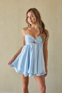 blue-image | Woman wearing a light blue dress with a bow detail against a beige background