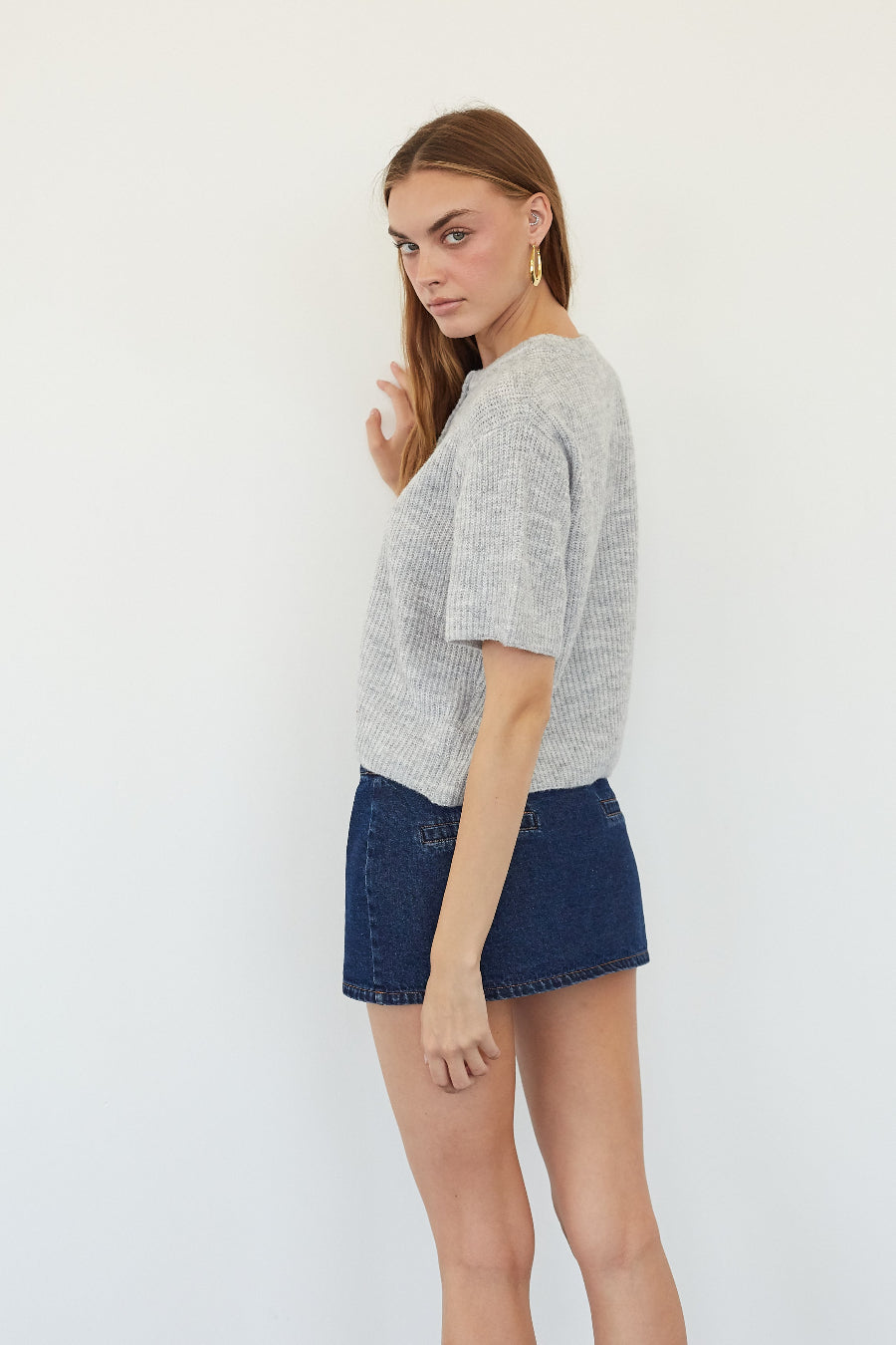 A woman modeling a light gray textured short-sleeve crop top and dark blue denim shorts against a plain white background.