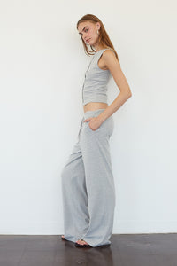 A woman modeling a matching two-piece loungewear set consisting of a sleeveless crop top and wide-leg pants, both in a light gray and white striped pattern, standing against a plain white wall.