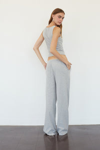 A woman modeling a matching two-piece loungewear set consisting of a sleeveless top and wide-leg pants, both in a light gray and white striped pattern, standing against a plain white wall.