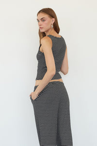 A woman stands in profile wearing a sleeveless black and white horizontally striped crop top and matching wide-leg pants against a plain white wall.