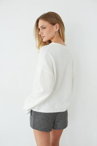 Woman wearing a white sweater and gray shorts on a plain background