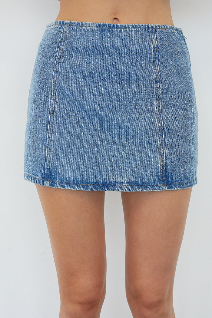 A light blue denim mini skirt worn by a model, shown from the waist down against a plain light gray background.