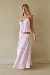 Woman wearing a pink ruffled top and skirt set against a beige wall.