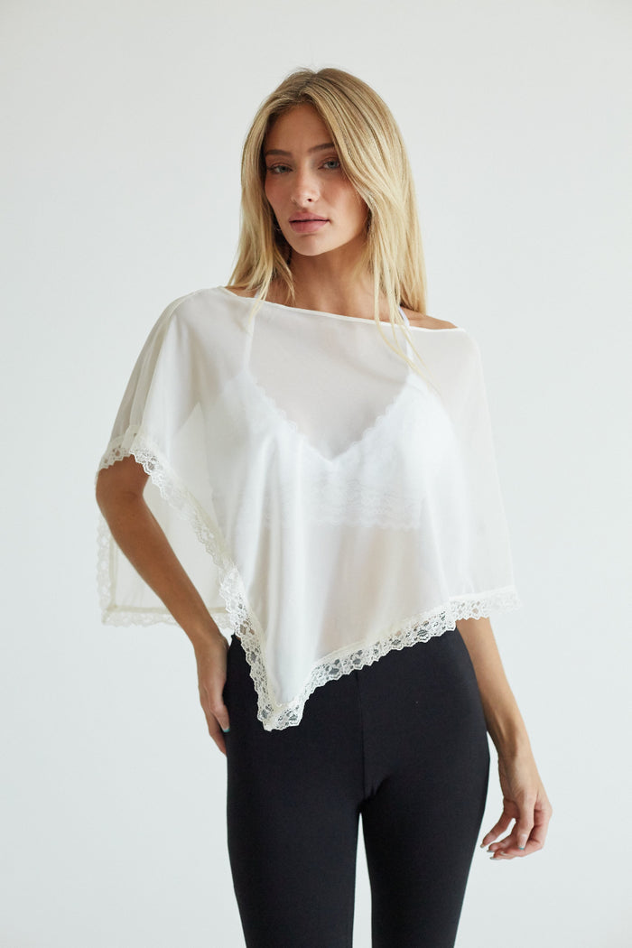 white-image | A blonde woman modeling a white sheer off-the-shoulder blouse with delicate lace trim, paired with black leggings, against a plain light gray studio background.