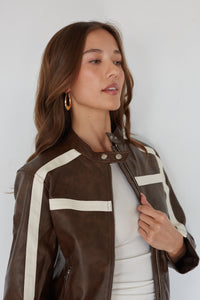 Woman wearing a brown leather jacket with white stripes against a white background