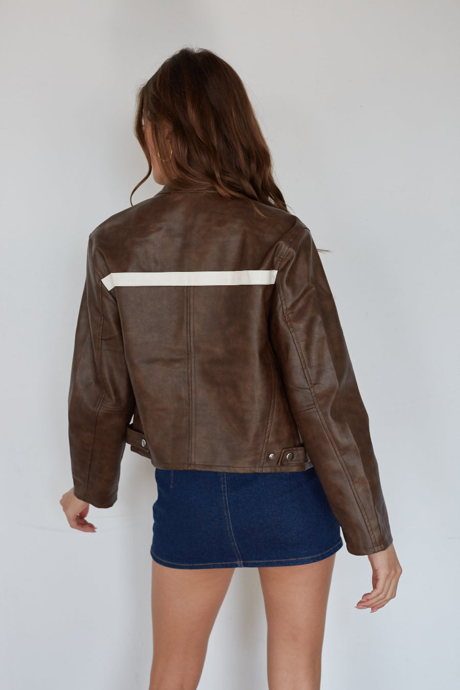 Person wearing a brown leather jacket with a white stripe on a plain background