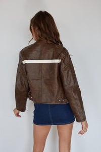 Person wearing a brown leather jacket with a white stripe on a plain background