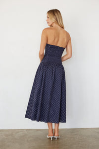 Woman wearing a strapless navy polka dot dress against a white background