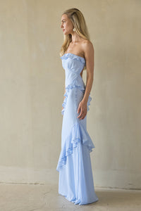 Woman wearing a light blue strapless gown with ruffled details against a beige background