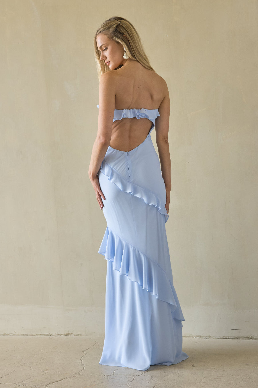 Woman wearing a light blue strapless dress with ruffled layers against a beige background