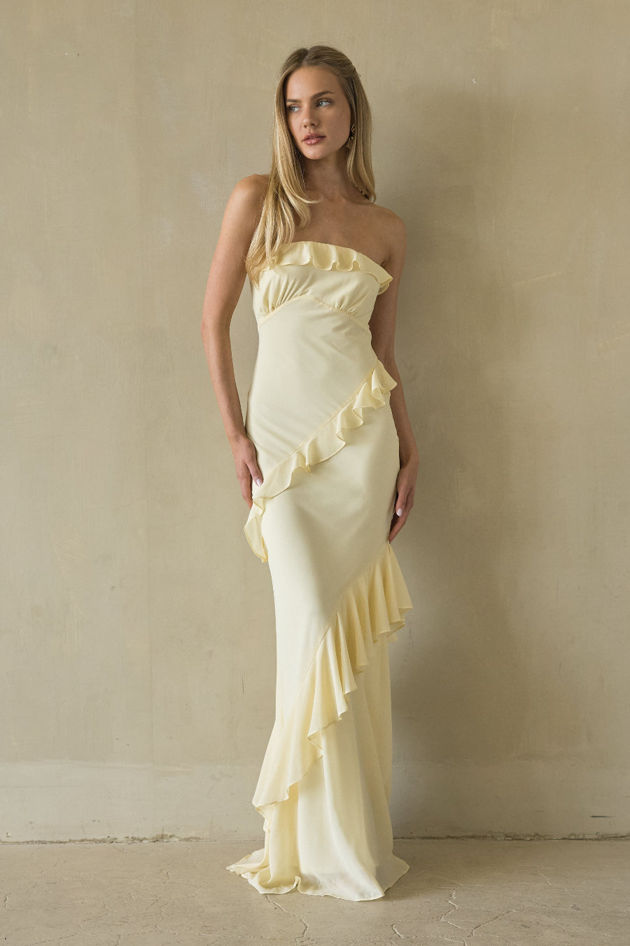yellow-image | Woman wearing a strapless, ruffled yellow dress against a plain wall.
