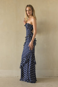 Woman wearing a strapless navy blue dress with white polka dots against a beige wall.