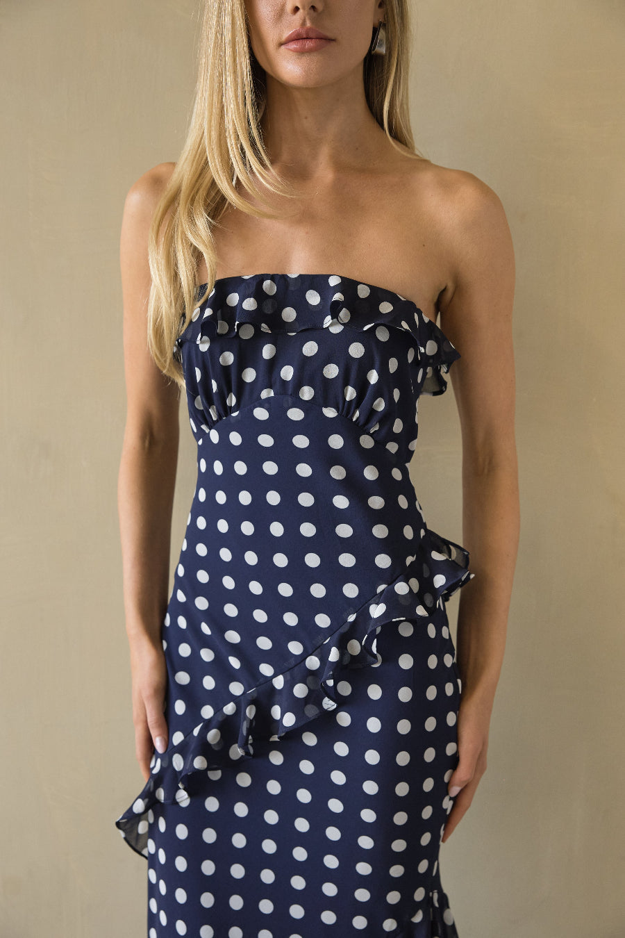 Woman wearing a strapless navy dress with white polka dots against a beige background
