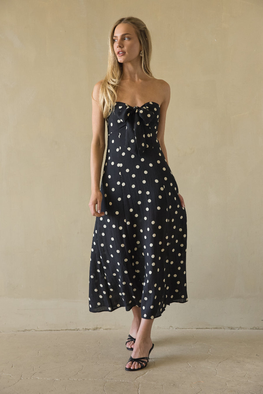 Woman wearing a black strapless dress with white polka dots against a beige background