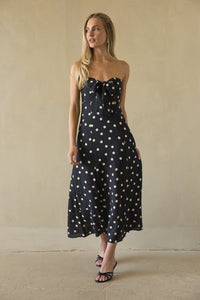 Woman wearing a black strapless dress with white polka dots against a beige background