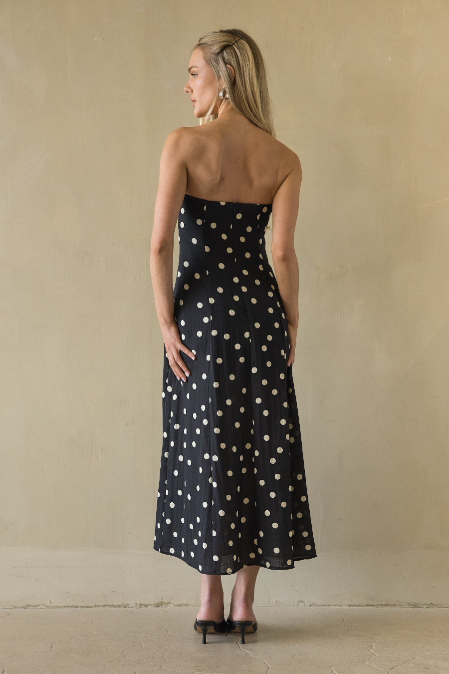Woman wearing a black strapless dress with white polka dots against a beige background