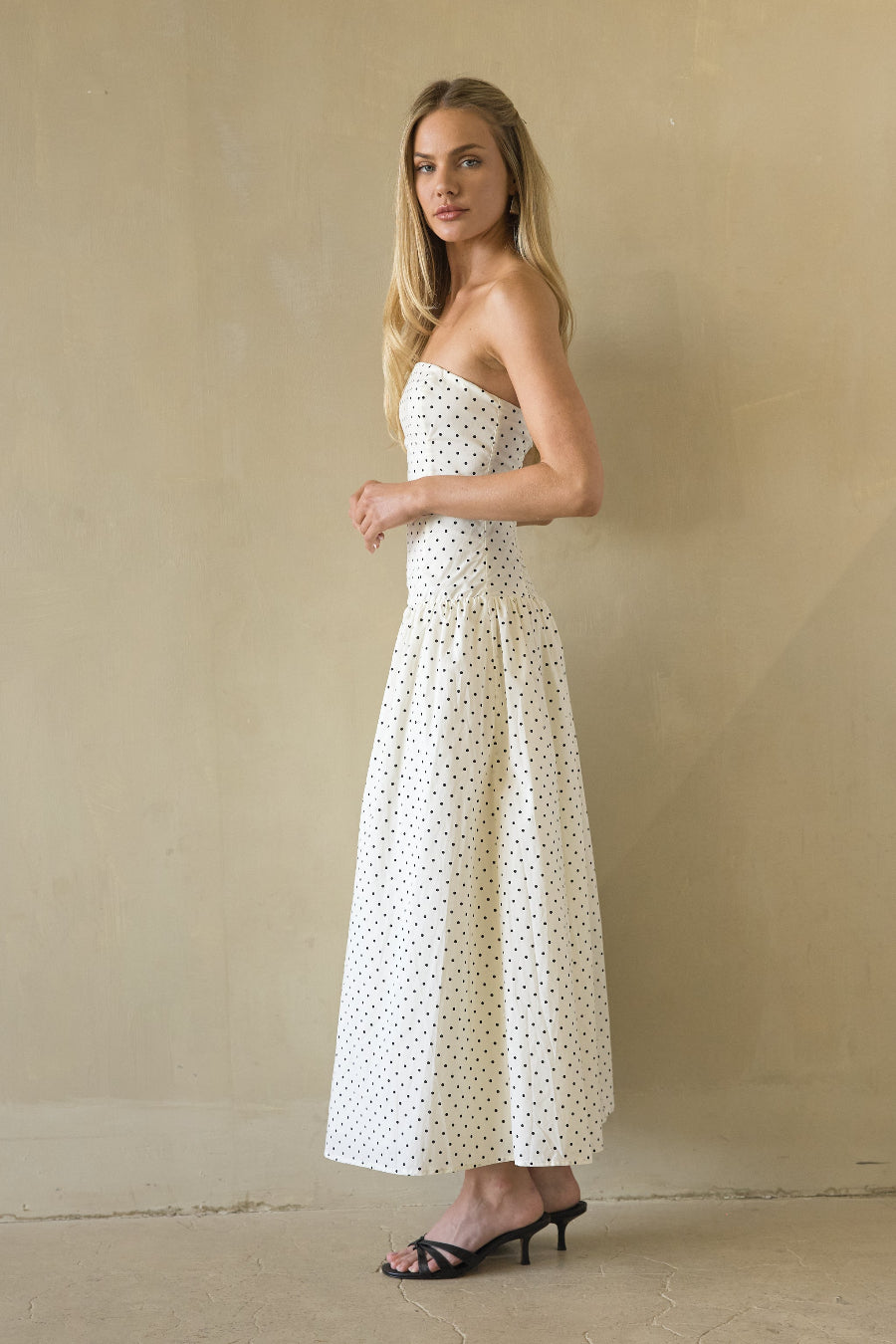 Woman wearing a strapless polka dot dress against a beige background