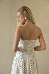 Woman wearing a strapless polka dot dress against a beige background