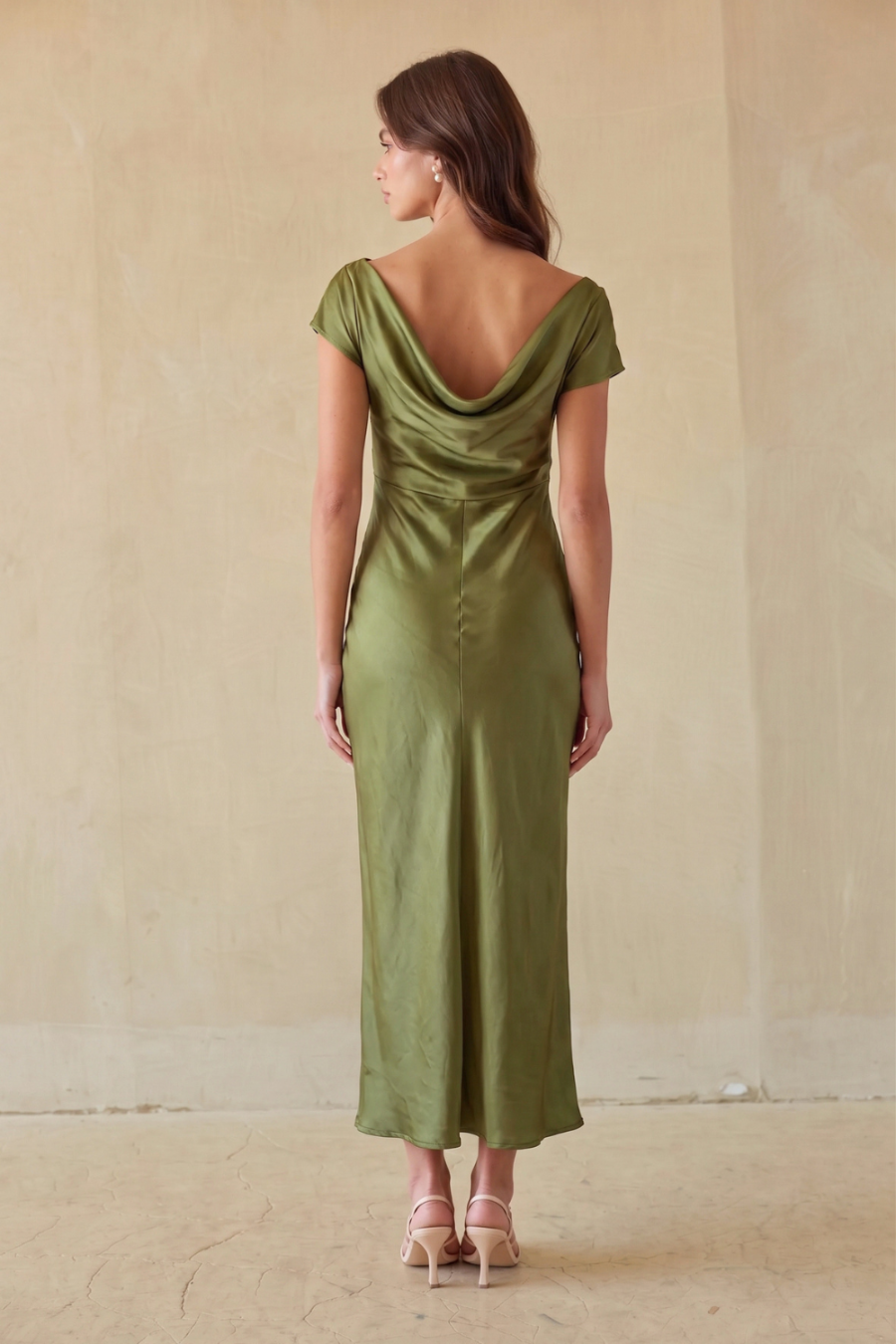 brunette model wearing an off the shoulder green dress against a beige wall.