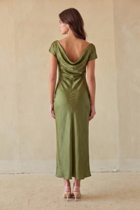 brunette model wearing an off the shoulder green dress against a beige wall.