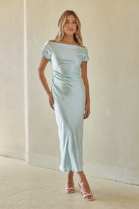 Woman wearing a light blue off-shoulder dress against a plain background