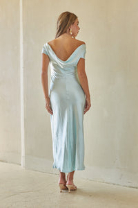 Woman wearing a light blue off-shoulder dress against a plain white wall.