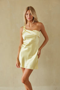 Woman wearing a light yellow one-shoulder dress against a beige background